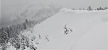 Large cornices looming over heavily wind-loaded slopes. Some mostly buried debris is barely visible on the slope below the largest cornice.