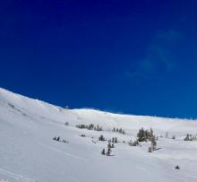 Strong E wind visibly blowing snow over the ridge