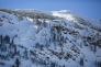 Upper bowl of Red Lake peak is visible with previous ski tracks. The lower part of the avalanche path is obscured by a small ridge line with trees. 